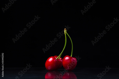 Three red cherries on a black background. Three cherries on one stalk. Ripe juicy cherries. only cherries on a black background
