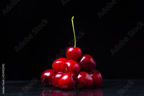 Red cherry pyramid. Red cherries folded in the form of a pyramid. At the very top is a cherry with a green stem. Cherry on a black background