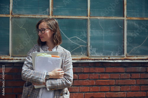 Fotografie Portrait of beautiful business woman in blazer standing in front of old new yorker building while holding some paperwork and documents ready for a professional and important meeting in town