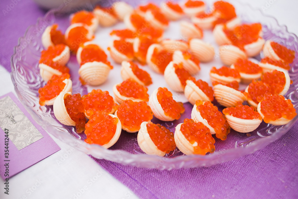 Canapes with caviar on a transparent plate in a bright space. Bright orange caviar and a lilac napkin under a transparent dish. Snack at the event.