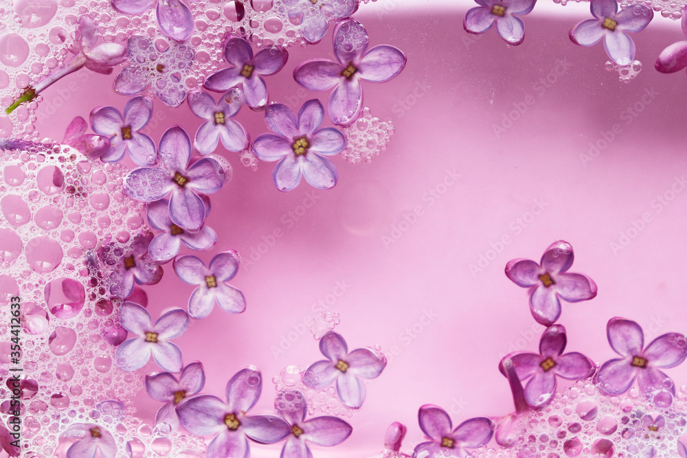 Background with soapy water with foam and lilac flowers. The fragrance of spring flowers. The scent of lilac. Spa treatment. Cleaning, Laundry. Background with soapy water with foam and lilac flowers. The fragrance of spring flowers. The scent of lilac. Spa treatment. Cleaning, Laundry.