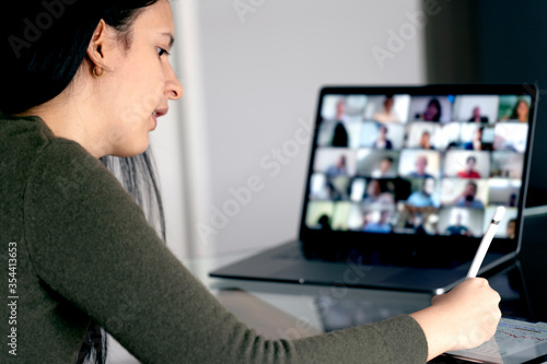 Woman in a video conference with her team taking notes. Working at home remotely with a laptop.