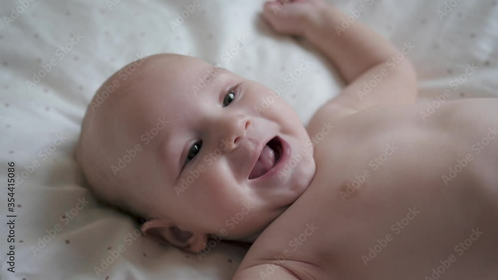 Close Up Portrait Of Funny Small Baby Smiling Playfully While Lying In White Bed Close Up Portrait Of Funny Small Baby Smiling Playfully While Lying In White Bed