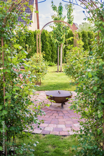 Traumhaft schöner grüner Garten mit Rosenbogen und Feuerplatz mit Feuerschale