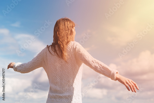 Woman stands with outstretched arms against the backdrop of a solar flare and blue sky