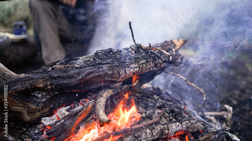 A male tourist trekker sitting near the bonfire to get warm  camping fire in the forest after long trekking  dinner time on the trek  warmth in the evening in the forest and mountains