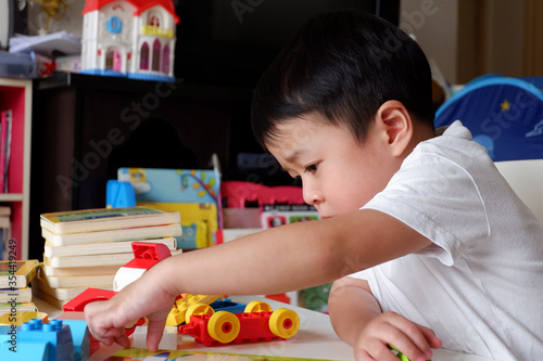 An Asian boy is playing a toy on a white table.