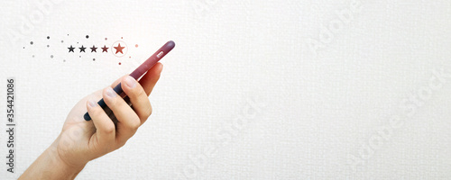 Close up of a person's hand holding a smartphone with an icon of a five star rating feedback on the concept of business service and services