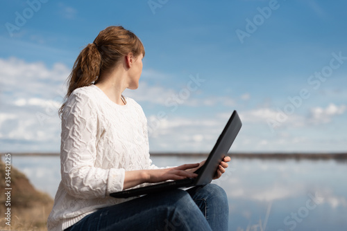 Woman looking to the side using laptop on the street, working remotely