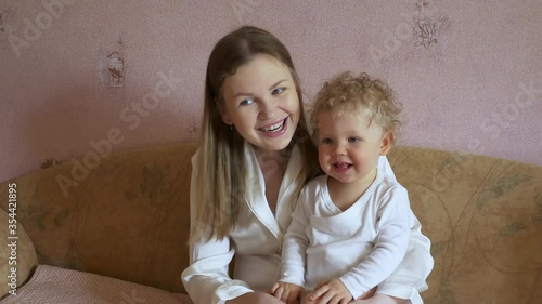 Beautiful attractive mother with a cute baby sits at home on the couch and has fun watching TV. Close-up.