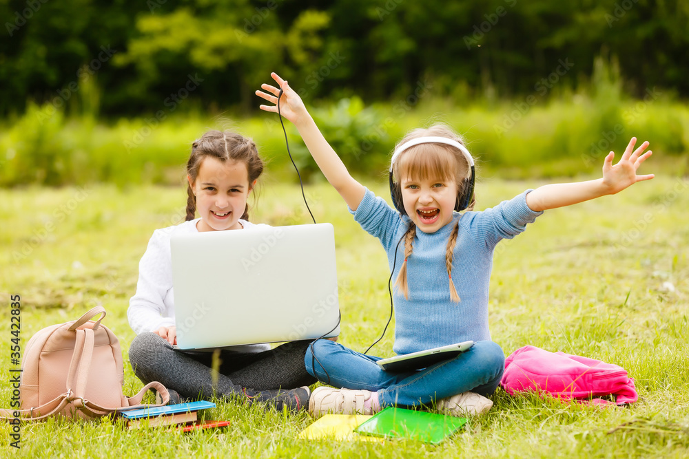 Fototapeta premium two funny schoolgirls sit on the grass and read books. Girls, girlfriends, sisters are taught lessons in nature.