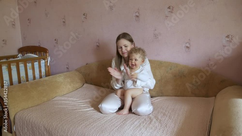 Beautiful attractive mother with a cute baby sits at home on the couch and has fun watching TV.