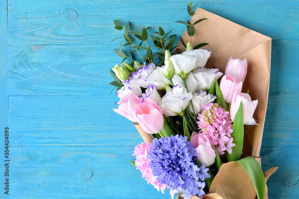 Trendy bouquet of flowers with pink tulips, elegant hyacinths and tender eustoma on blue wooden background. Romantic gift. Spring flowers. 