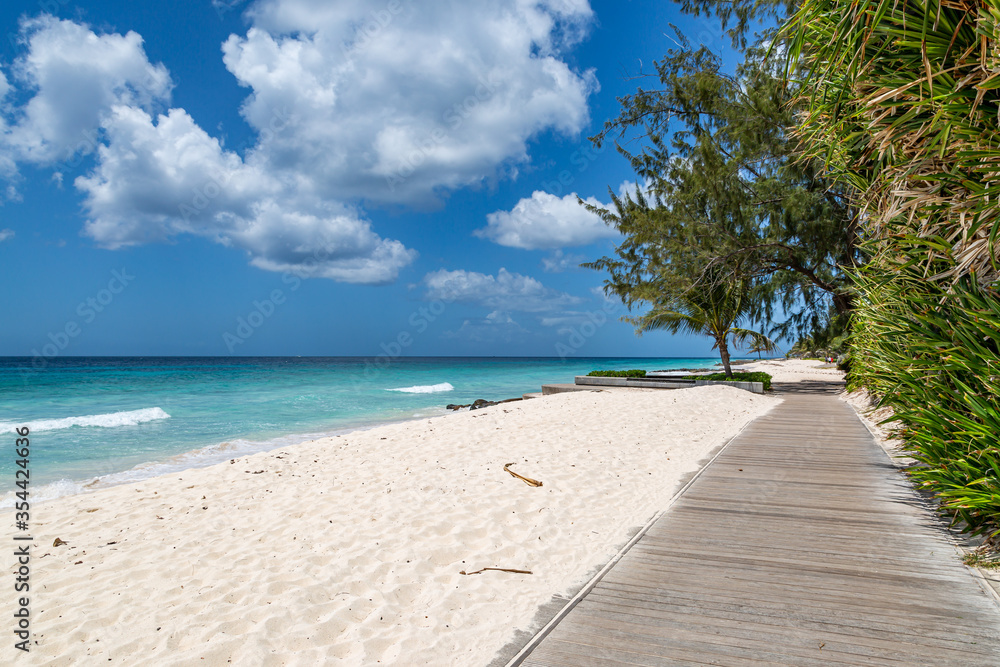 Looking along a wooden boardwalk running alongside a sandy Caribbean beach