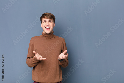 young blonde man looking desperate and frustrated, stressed, unhappy and annoyed, shouting and screaming isolated against flat wall photo