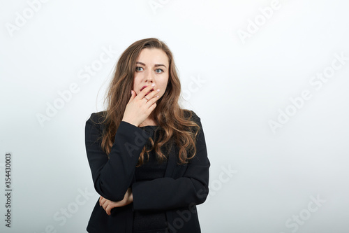 Young Attractive Woman Brunette In In Black T-Shirt And Sweater On White Background, Terrified Woman Covers Mouth With Her Hand As Sign Of Fear. Surprise, A Person Is Afraid