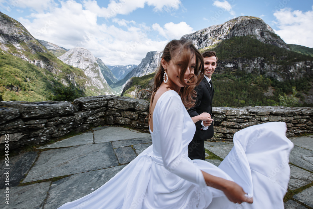 Naklejka premium newlyweds running together on a stone path against the background of mountains