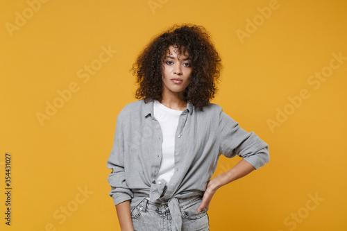 Young african american woman girl in gray casual clothes posing isolated on yellow background studio portrait. People emotions lifestyle concept. Mock up copy space. Standing with arm akimbo on waist.