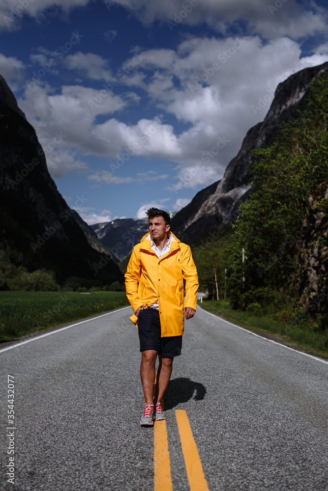A tourist in a yellow raincoat walks along the highway A tourist in a yellow raincoat walks along the highway