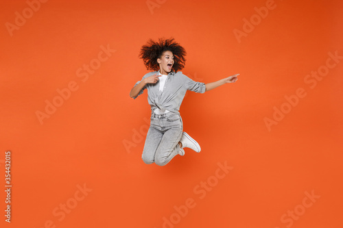 Excited young african american woman girl in gray casual clothes posing isolated on orange background studio portrait. People lifestyle concept. Mock up copy space. Jumping, point index fingers aside.