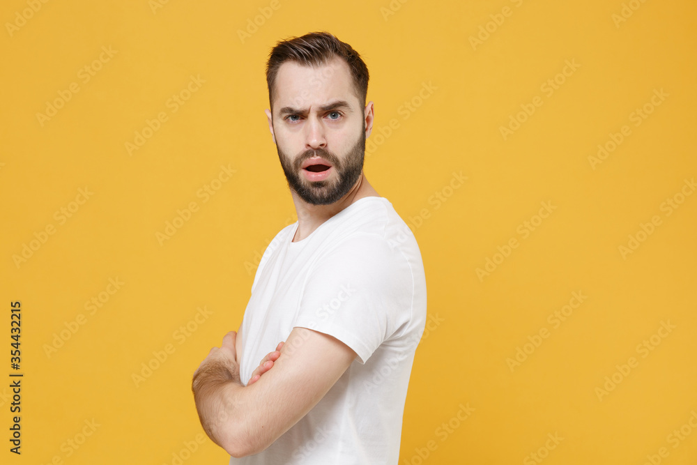 Side view of shocked perplexed young bearded man guy in white casual t-shirt posing isolated on yellow background. People lifestyle concept. Mock up copy space. Holding hands crossed looking camera. Side view of shocked perplexed young bearded man guy in white casual t-shirt posing isolated on yellow background. People lifestyle concept. Mock up copy space. Holding hands crossed looking camera.