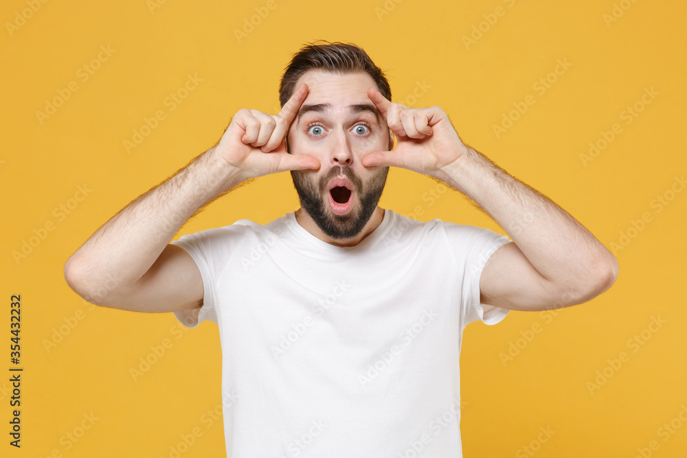 Shocked young bearded man guy in white casual t-shirt posing isolated on yellow wall background studio portrait. People lifestyle concept. Mock up copy space. Stretching eyelids, keeping mouth open. Shocked young bearded man guy in white casual t-shirt posing isolated on yellow wall background studio portrait. People lifestyle concept. Mock up copy space. Stretching eyelids, keeping mouth open.