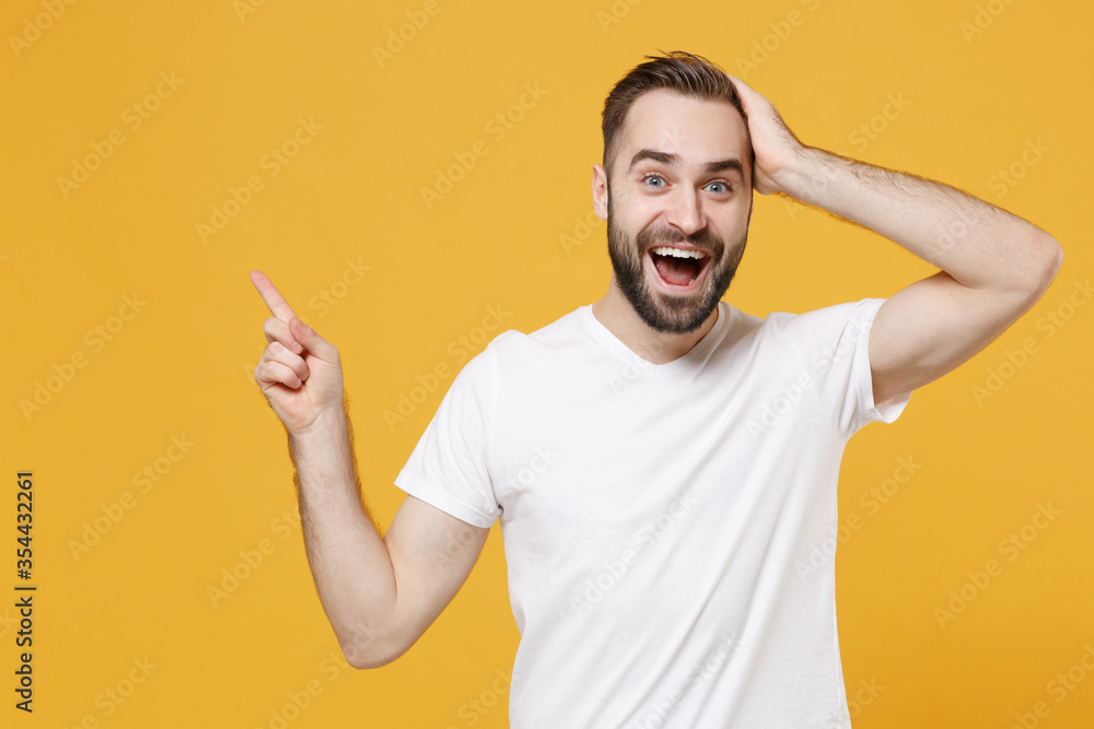 Excited young bearded man guy in white casual t-shirt posing isolated on yellow background studio portrait. People lifestyle concept. Mock up copy space. Pointing index finger up, put hand on head. Excited young bearded man guy in white casual t-shirt posing isolated on yellow background studio portrait. People lifestyle concept. Mock up copy space. Pointing index finger up, put hand on head.