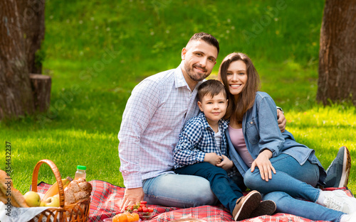 Happy parents with their little son on picnic in green park, copy space