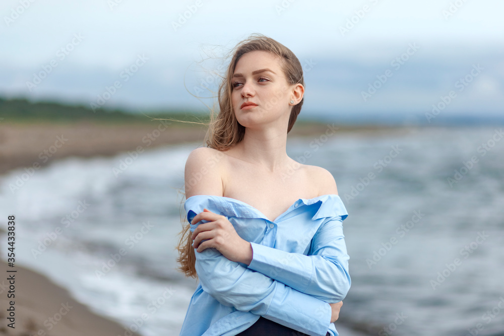 Beautiful young blonde girl in a blue shirt relaxing on the sea