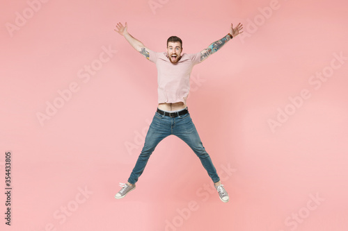 Excited young tattooed man guy in pastel casual t-shirt posing isolated on pink background studio portrait. People emotions lifestyle concept. Mock up copy space. Jumping spreading hands and legs.