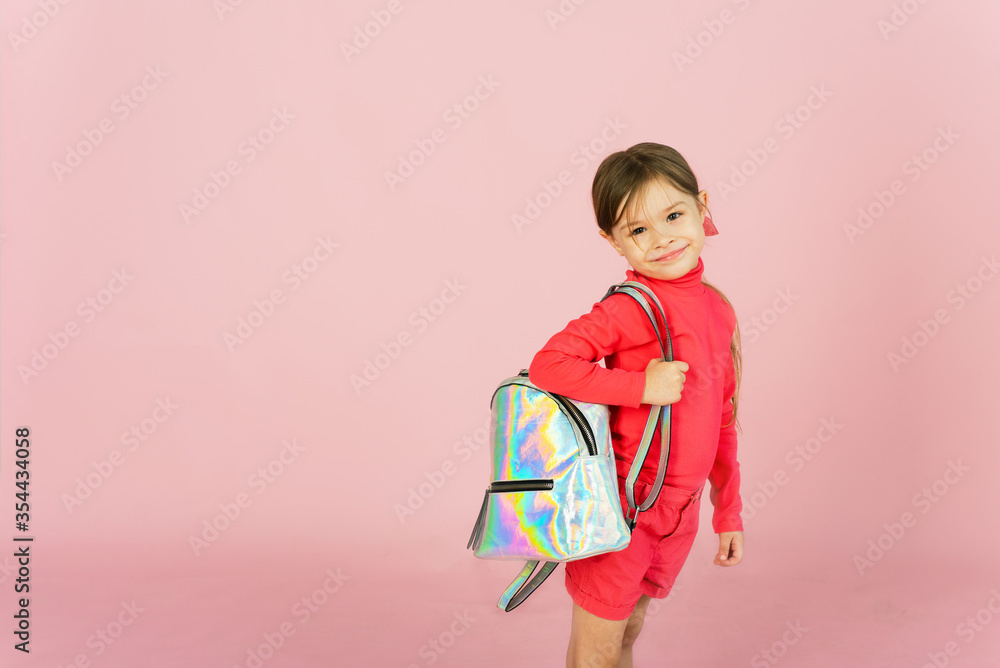Cute little blonde classmate in a pink suit in the studio with a holographic backpack. Funny first grader on a pink pastel background with copyspace Cute little blonde classmate in a pink suit in the studio with a holographic backpack. Funny first grader on a pink pastel background with copyspace