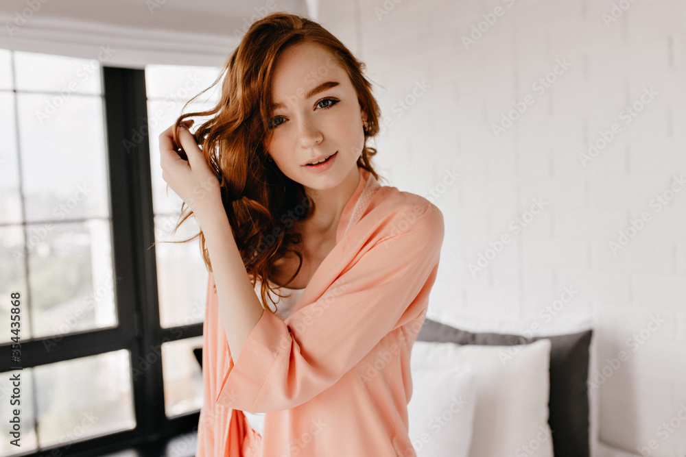 Gorgeous red-haired woman with cute smile posing at home. Graceful european girl standing in her flat. Gorgeous red-haired woman with cute smile posing at home. Graceful european girl standing in her flat.