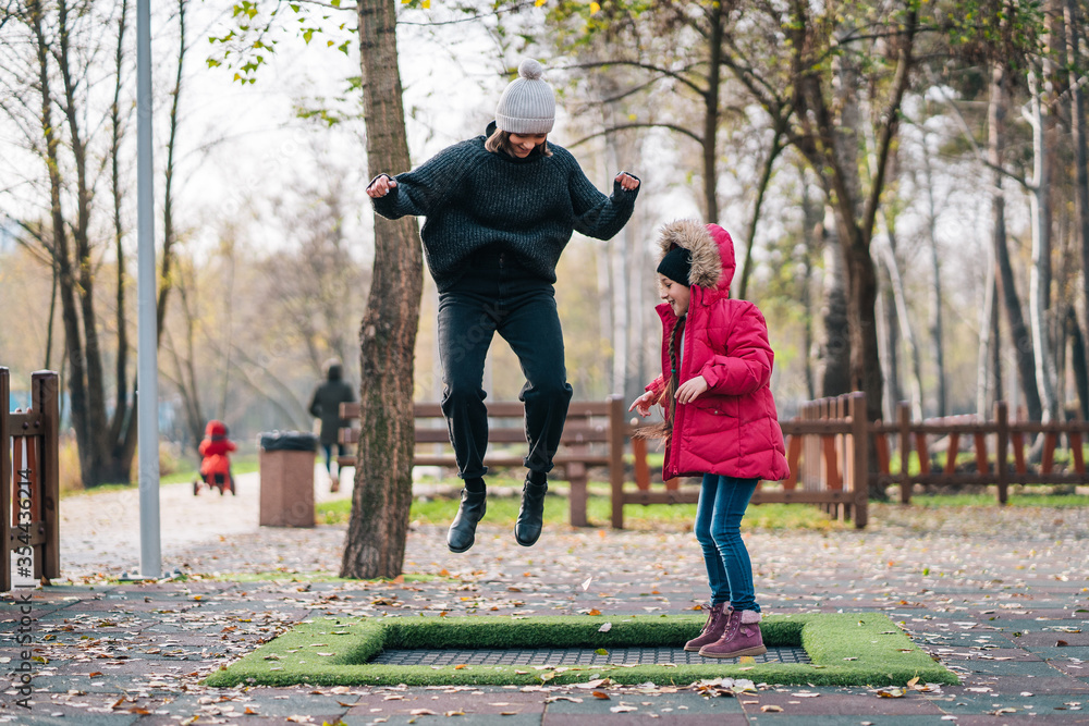 Fototapeta premium Mom and her daughter jumping together on trampoline in autumn park