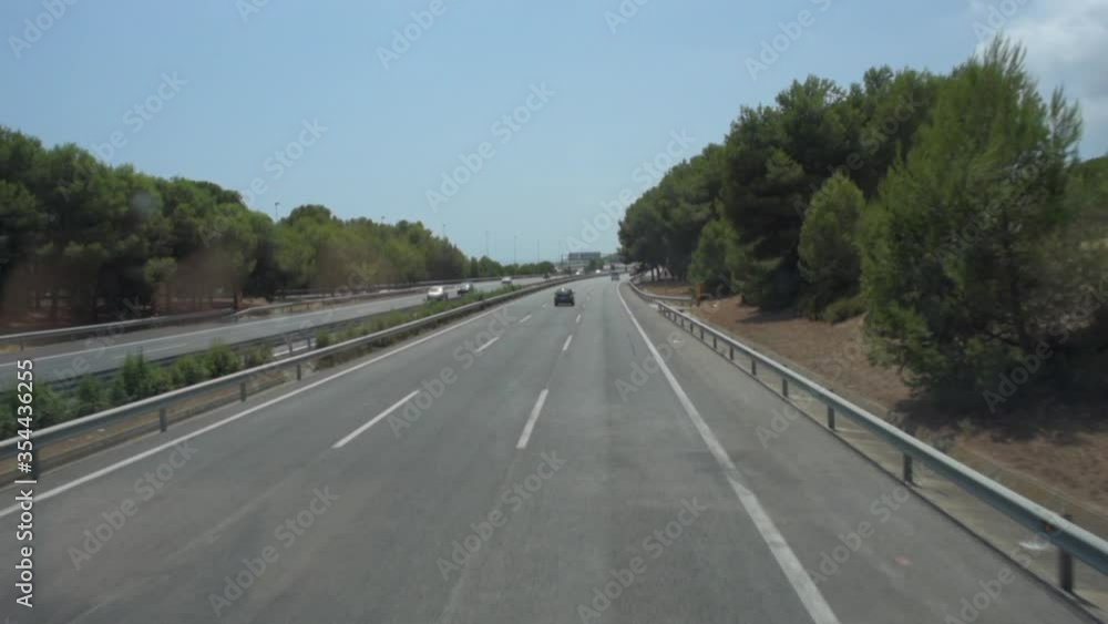 POV shot of vehicles on road amidst trees against sky during sunny day - Barcelona, Spain POV shot of vehicles on road amidst trees against sky during sunny day - Barcelona, Spain