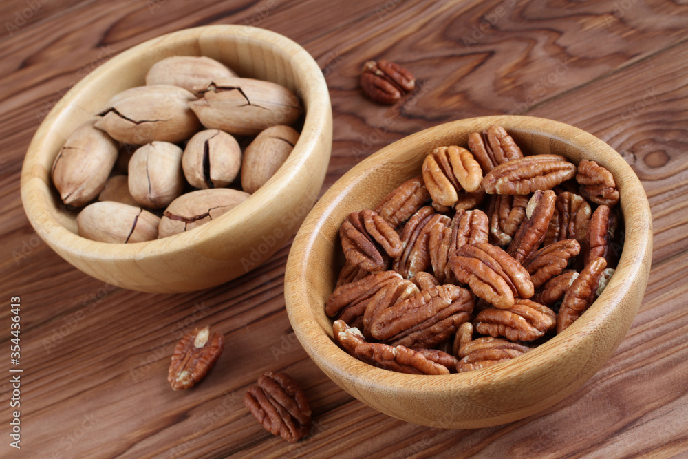 Peeled pecan nuts and unpeeled pecan nuts in bamboo bowls on wooden background