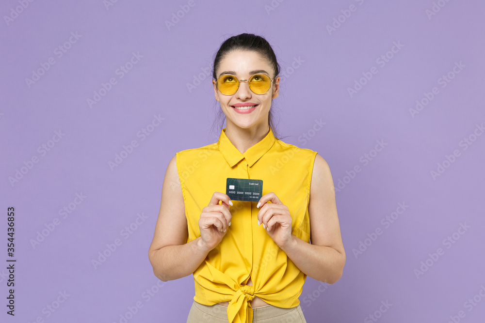 Pensive young brunette woman girl in yellow casual shirt posing isolated on violet background studio portrait. People emotions lifestyle concept. Mock up copy space. Hold credit bank card, looking up. Pensive young brunette woman girl in yellow casual shirt posing isolated on violet background studio portrait. People emotions lifestyle concept. Mock up copy space. Hold credit bank card, looking up.
