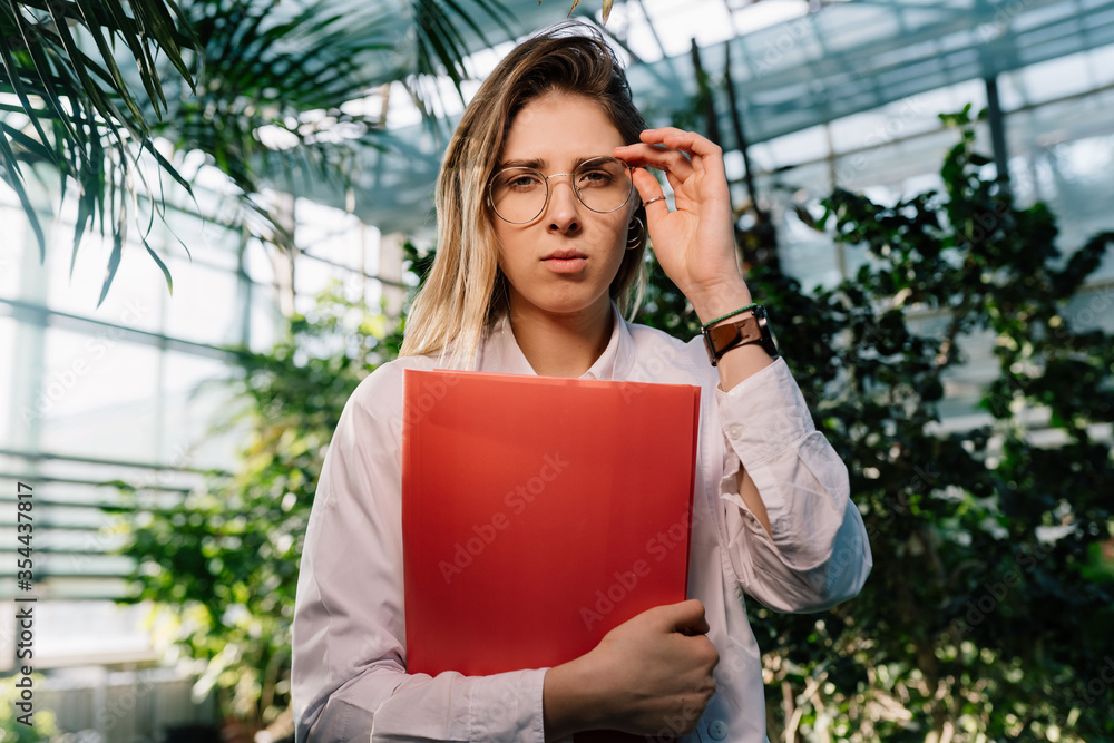 Fototapeta premium Young agricultural engineer working in greenhouse. Young female scientist looking at the camera