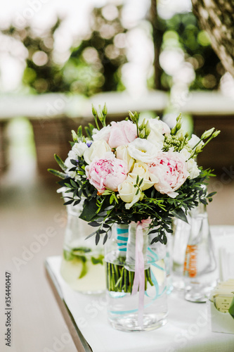 Lovely white peony blooming flowers in glass vase on a white table. Floral composition, scene, daylight.