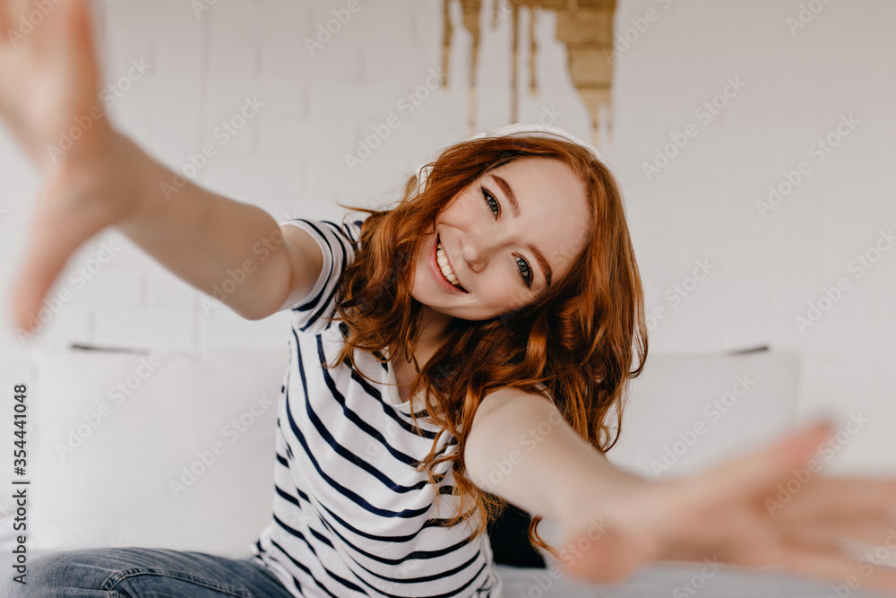 Ecstatic red-haired girl making selfie and laughing. Emotional caucasian lady in casual attire expressing happiness.