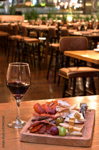Tabla de quesos y carnes frías acompañada con copa de vino tinto sobre mesa de madera en restaurante