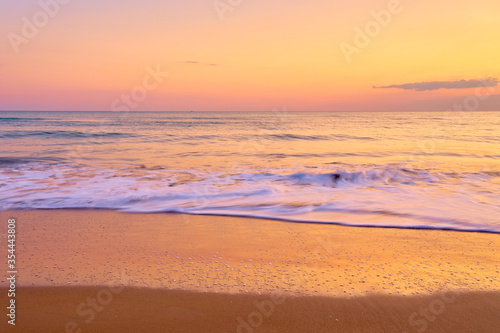 Colorful sunset at the tropical beach  sun behind clouds reflects on water and waves with foam hitting sand.