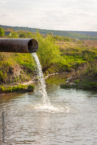 water flows from a pipe into a river against the backdrop of nature. The concept of nature pollution, the release of waste into the water