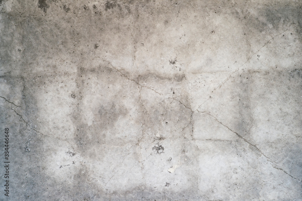 Grey concrete wall with cracks, rough surface and uneven color tone. Background