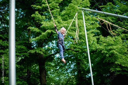 The girl is jumping on a bungee trampoline. A child with insurance and stretchable rubber bands hangs against the sky. The concept of happy childhood and games in the amusement park