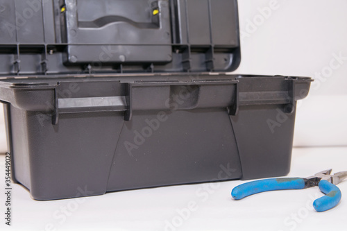 An open gray tool box stands on a white background, and nearby are pliers