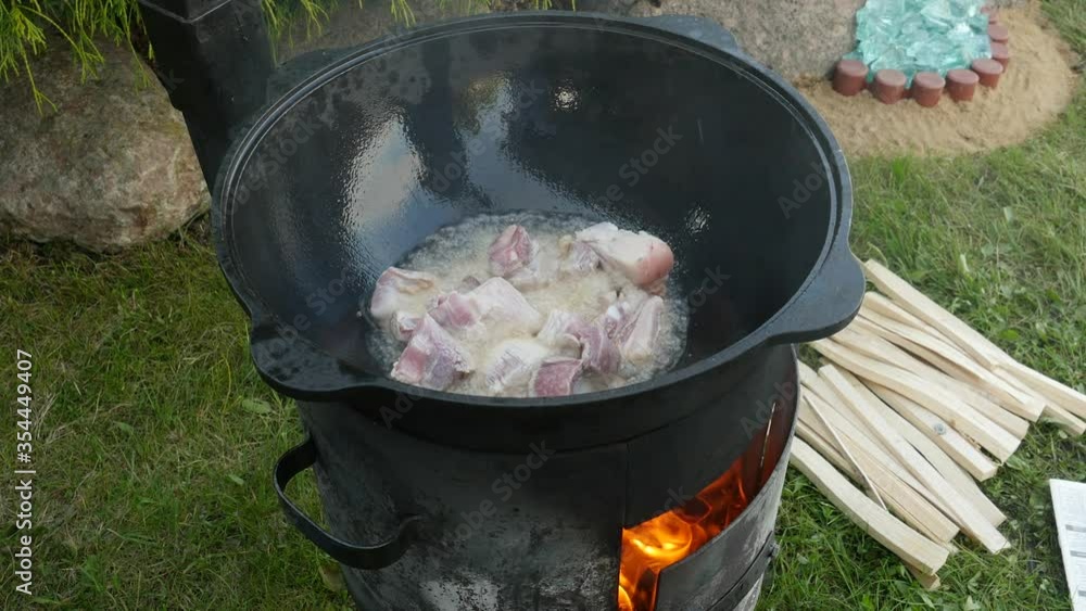 Cooking process, frying pork meat in large cauldron on open fire Cooking process, frying pork meat in large cauldron on open fire