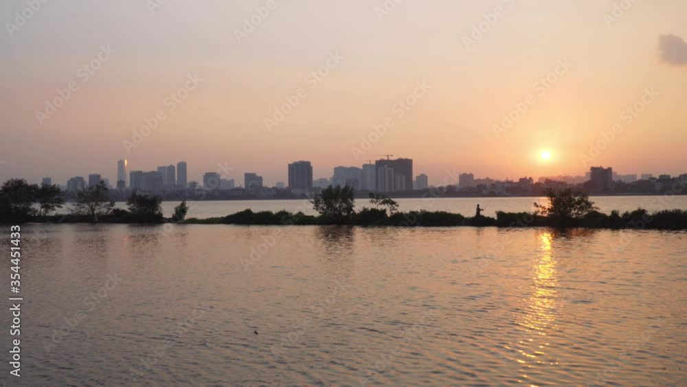 Hanoi - Sunset in West Lake with fisherman in silhouette Hanoi - Sunset in West Lake with fisherman in silhouette