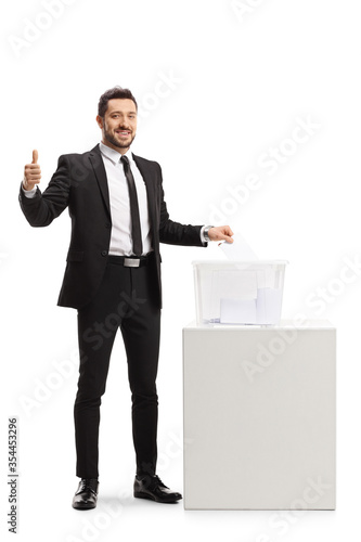 Businessman in a suit casting a vote in a ballot box and showing thumbs up photo