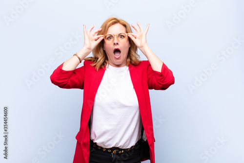 middle age woman feeling shocked, amazed and surprised, holding glasses with astonished, disbelieving look photo