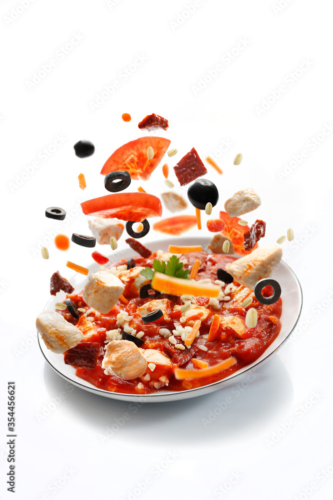 Chicken in tomato sauce with vegetables. Ready dish on a plate, fresh vegetables fall into the plate. Chicken in tomato sauce with vegetables. Ready dish on a plate, fresh vegetables fall into the plate.